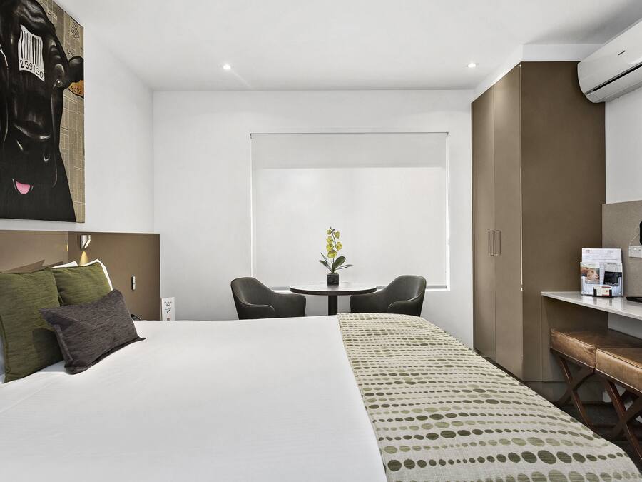 A modern hotel room with a large bed, a desk, and a small table with chairs.