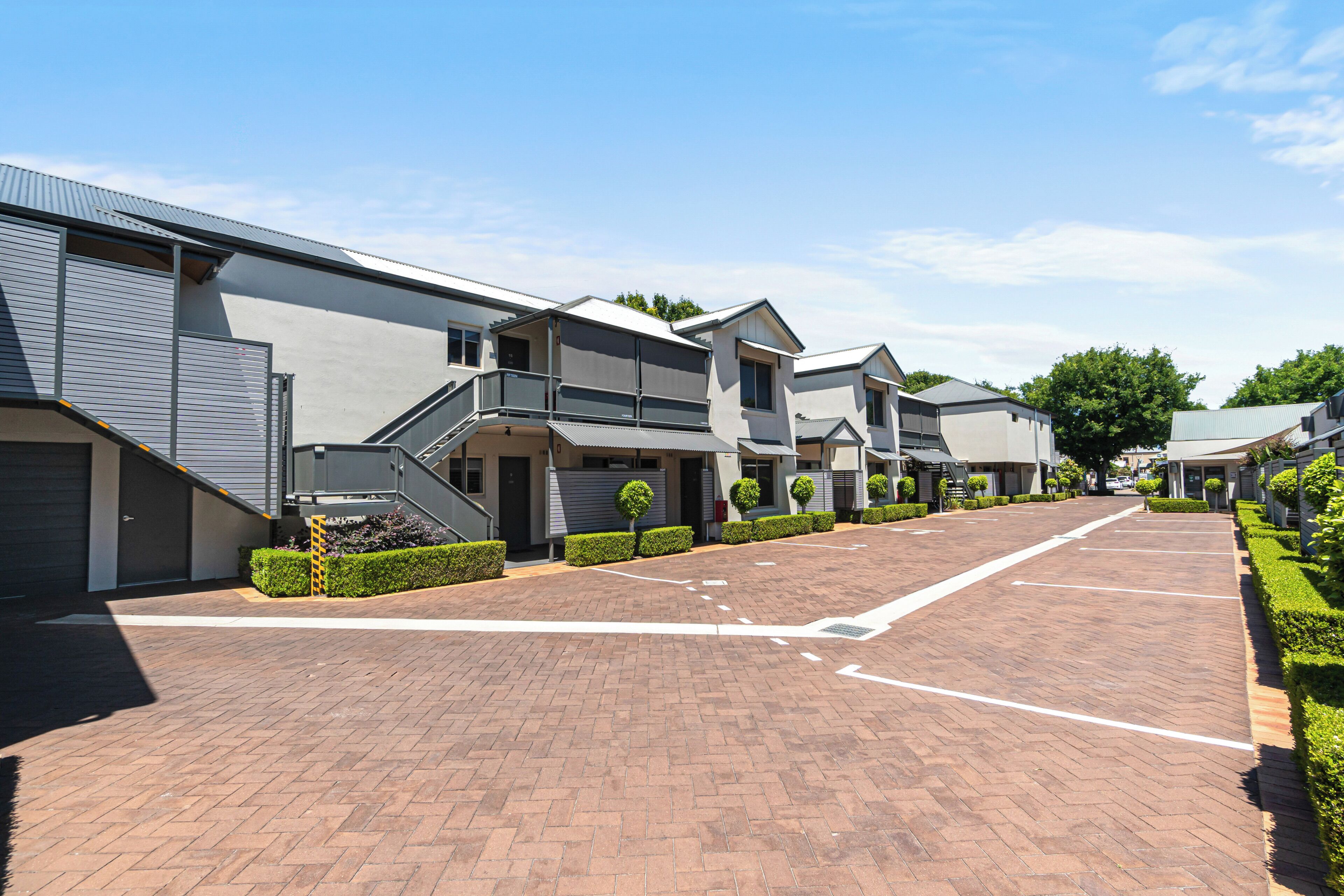 A modern building with a brick driveway, multiple garage doors, and neatly trimmed hedges.