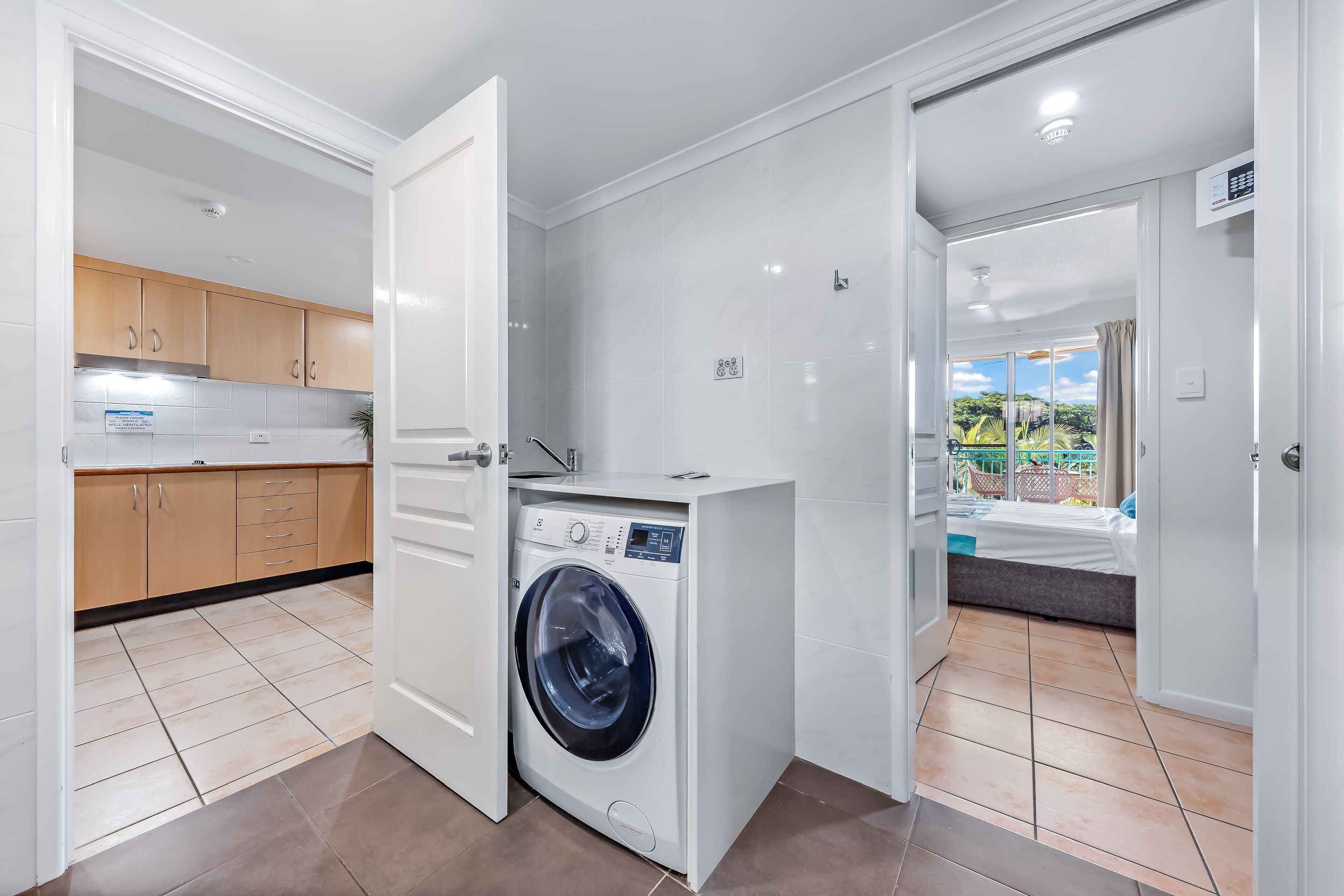 A compact apartment with a washing machine, a kitchenette, and a bedroom with a view.