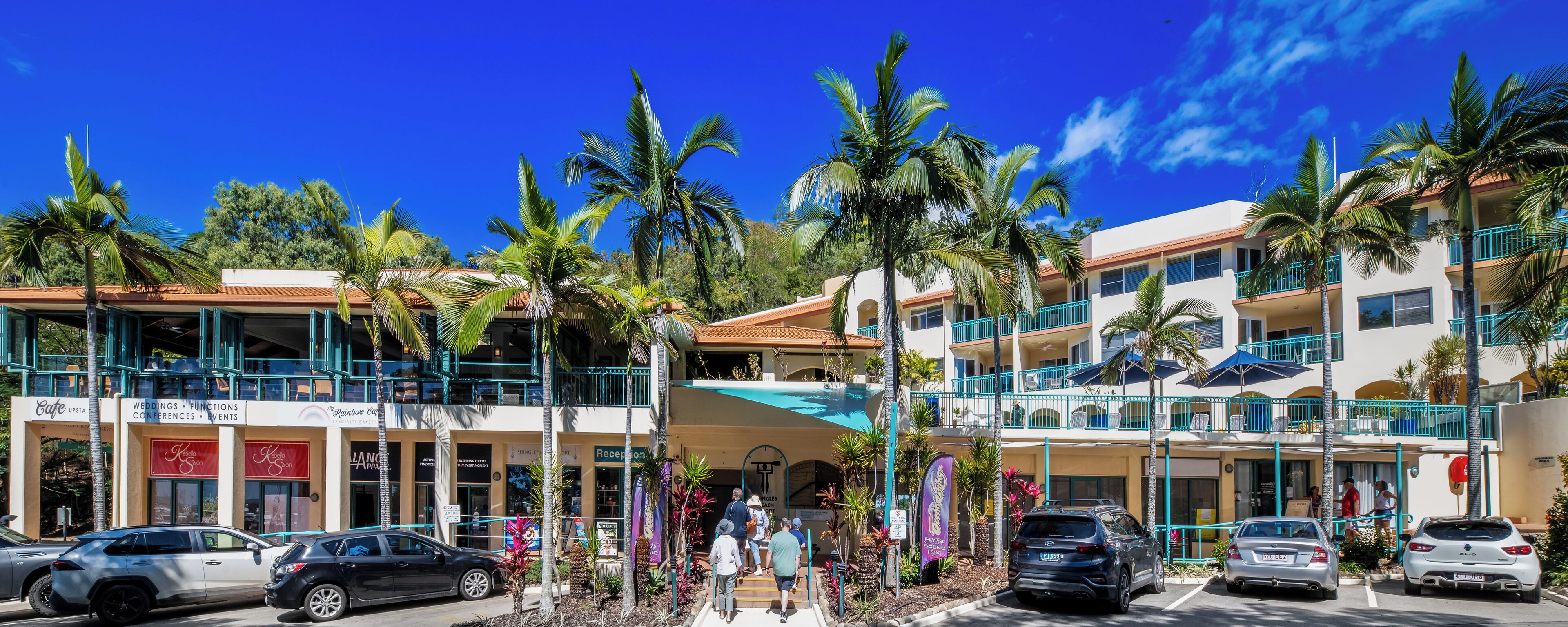 A hotel with multiple floors, outdoor seating, and palm trees.