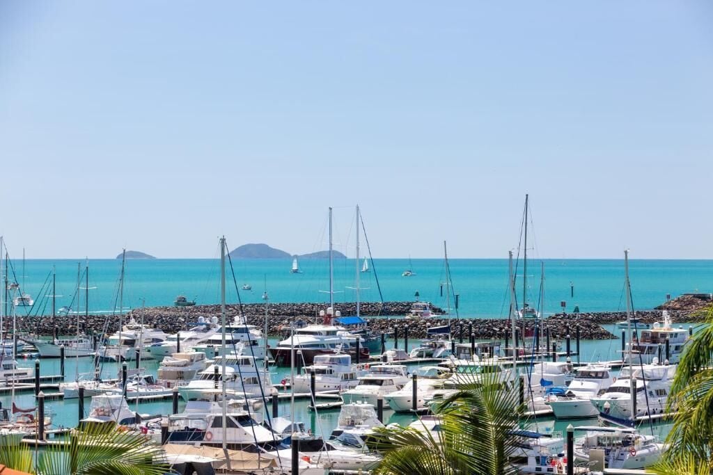 Un port de plaisance où de nombreux bateaux sont amarrés, un ciel dégagé et une mer calme.