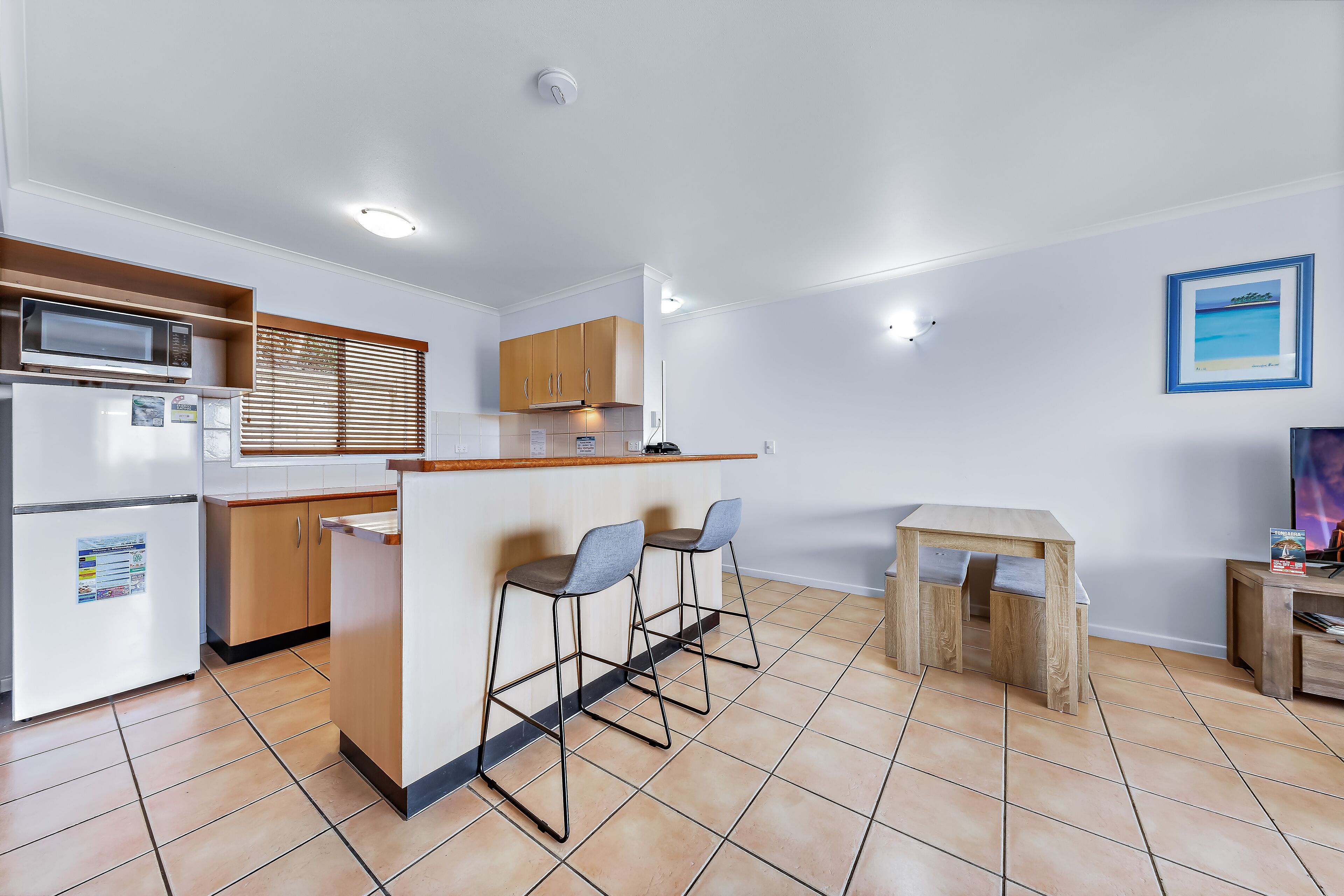 A modern kitchen with a central island, bar stools, a small wooden table, and a microwave.