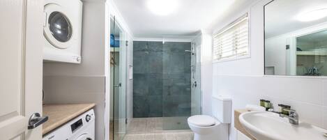 A modern bathroom with a washing machine, toilet, and sink.