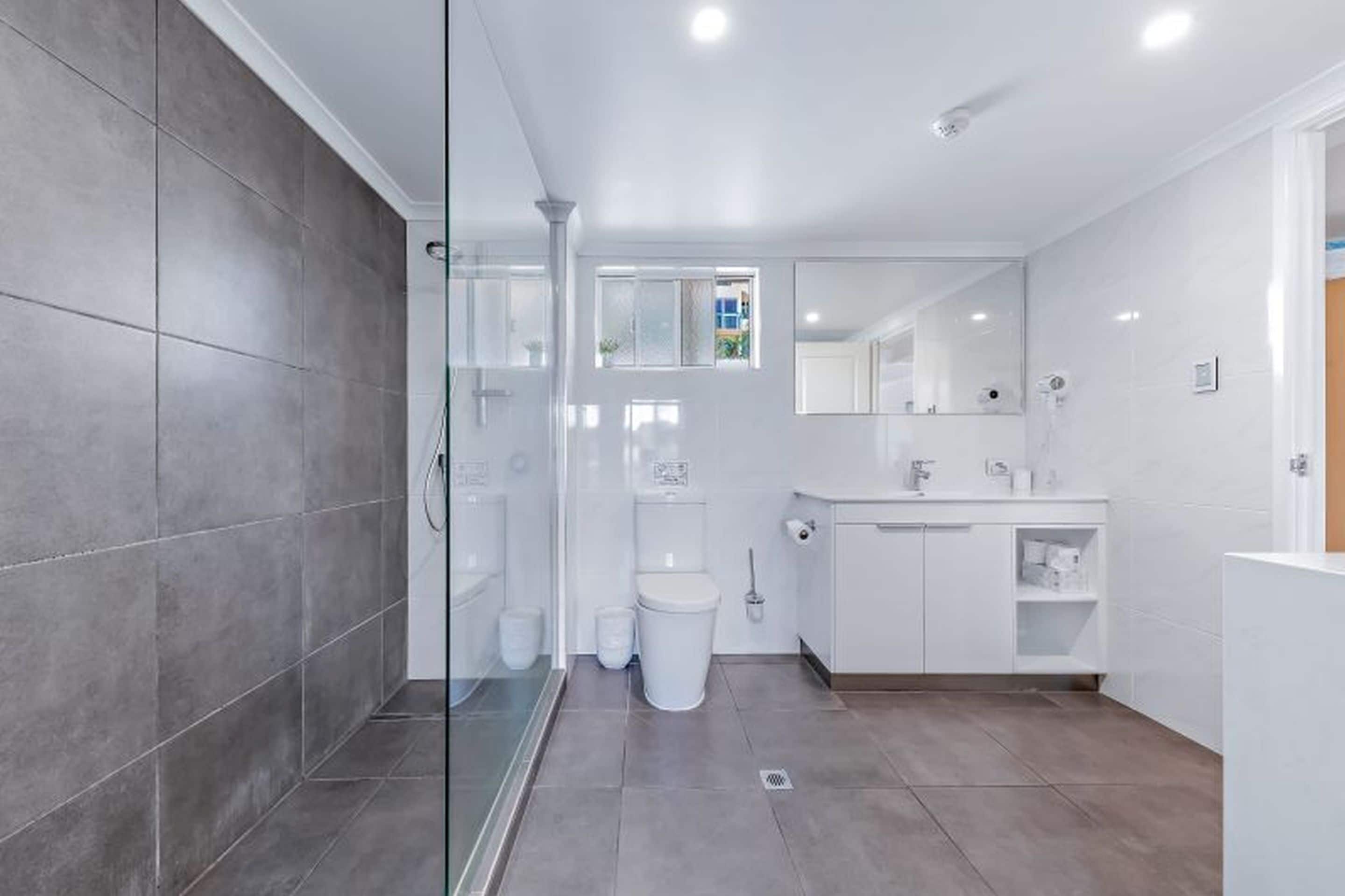 A modern bathroom with a glass shower enclosure, a toilet, and a sink with a mirror above.