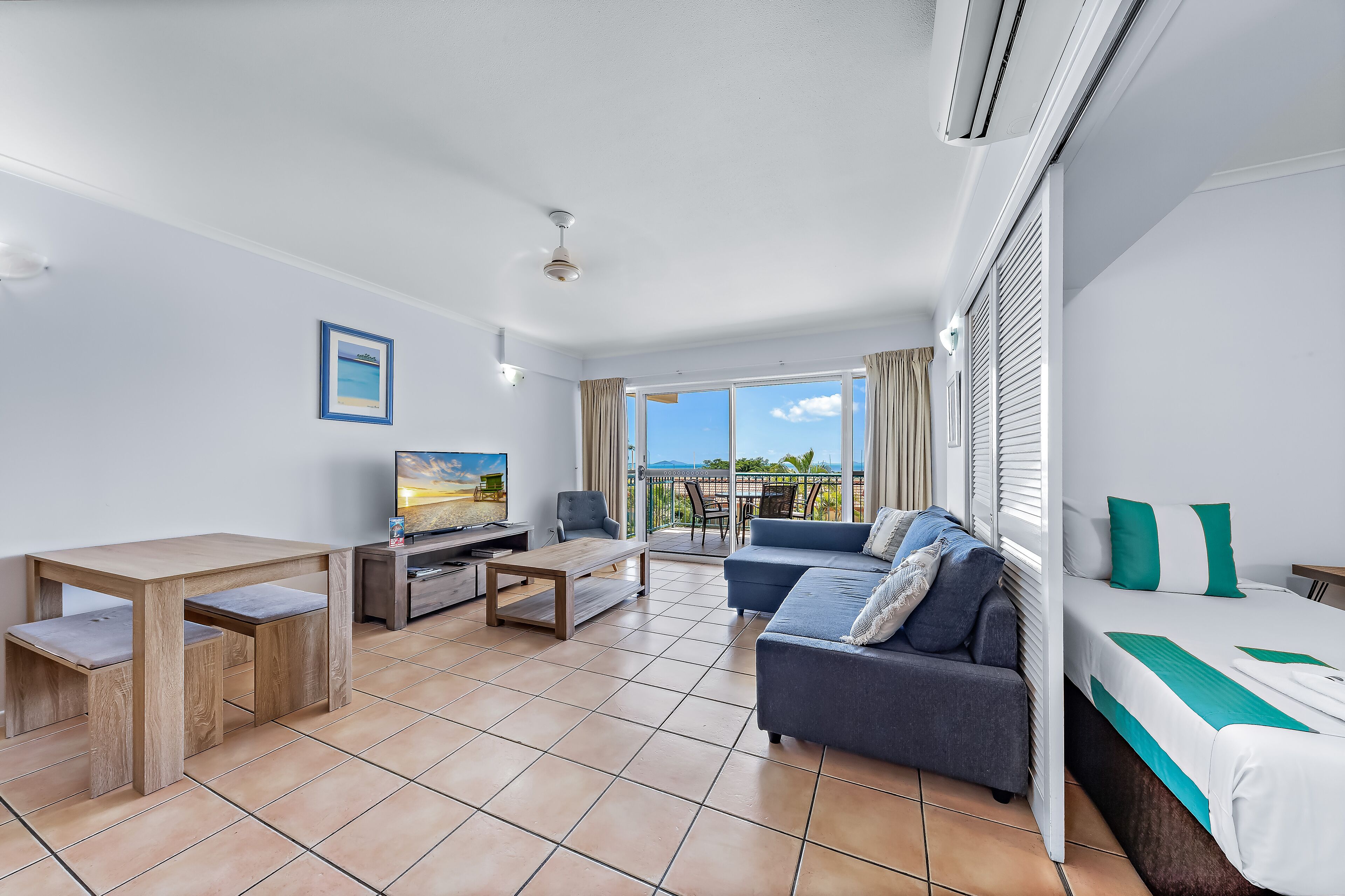 A modern hotel room with a balcony, a sofa, a dining table, and a TV.