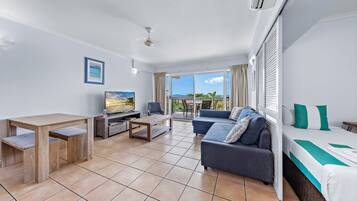 A modern hotel room with a balcony, a sofa, a dining table, and a TV.