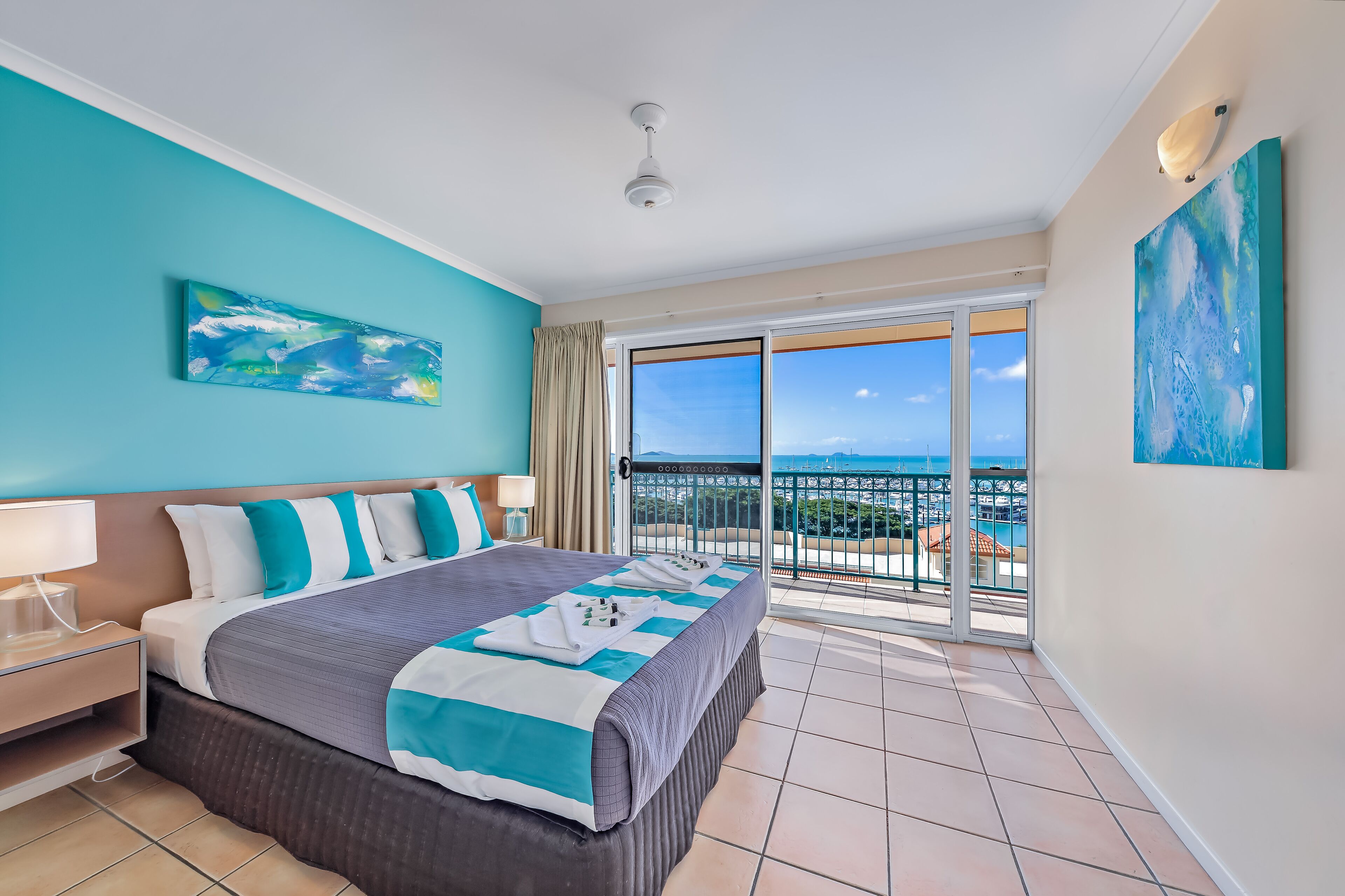 A hotel room with a large bed, a nightstand, a lamp, a painting, and a balcony with a view.