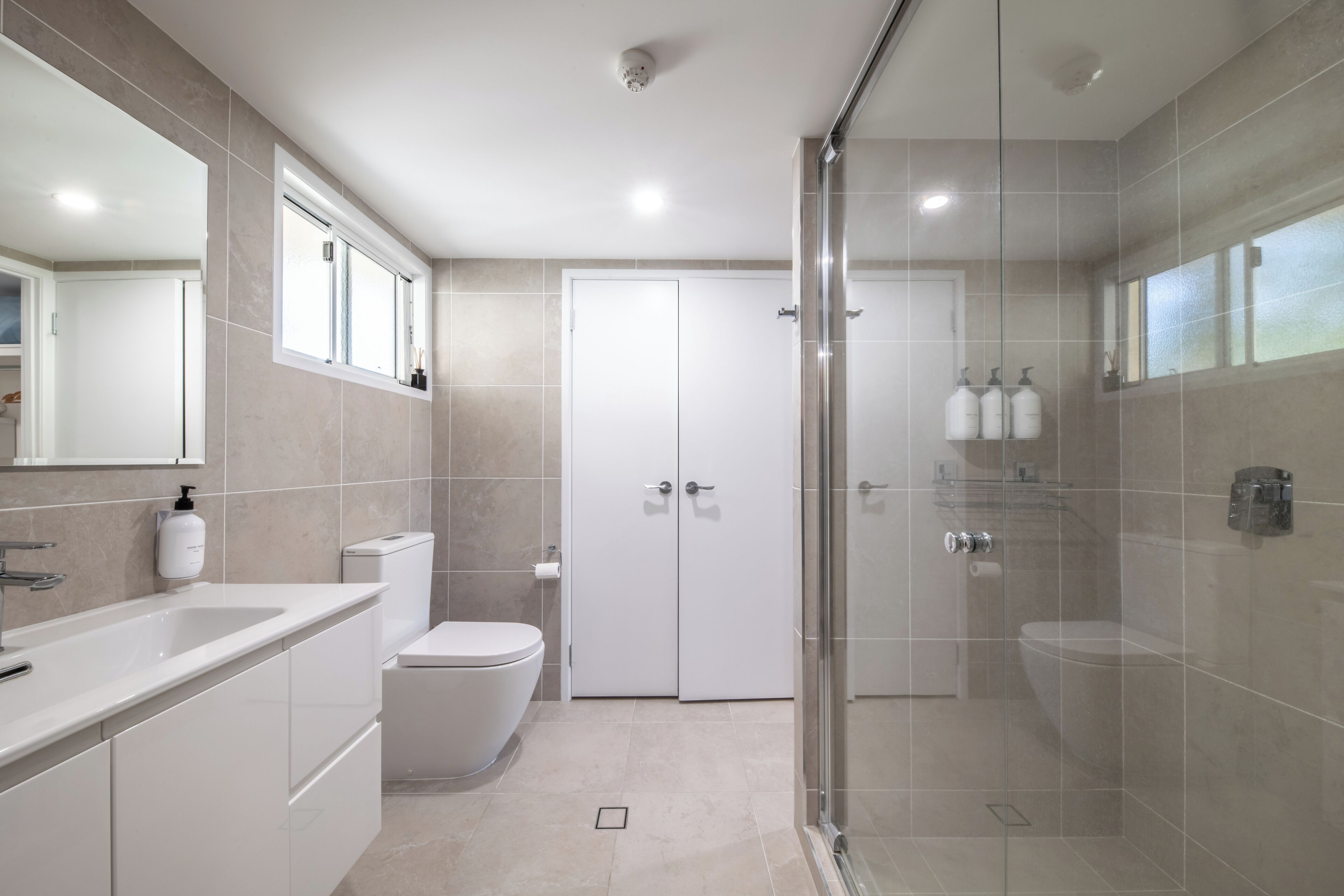A modern bathroom with a glass-enclosed shower, a white toilet, and a large mirror above the sink.