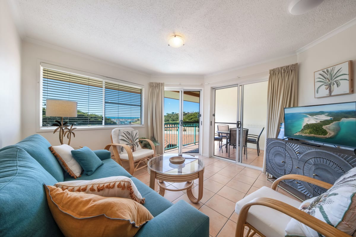 A living room with a sofa, chairs, a TV, and a balcony with a view.
