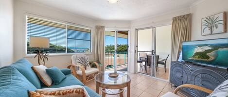 A living room with a sofa, chairs, a TV, and a balcony with a view.