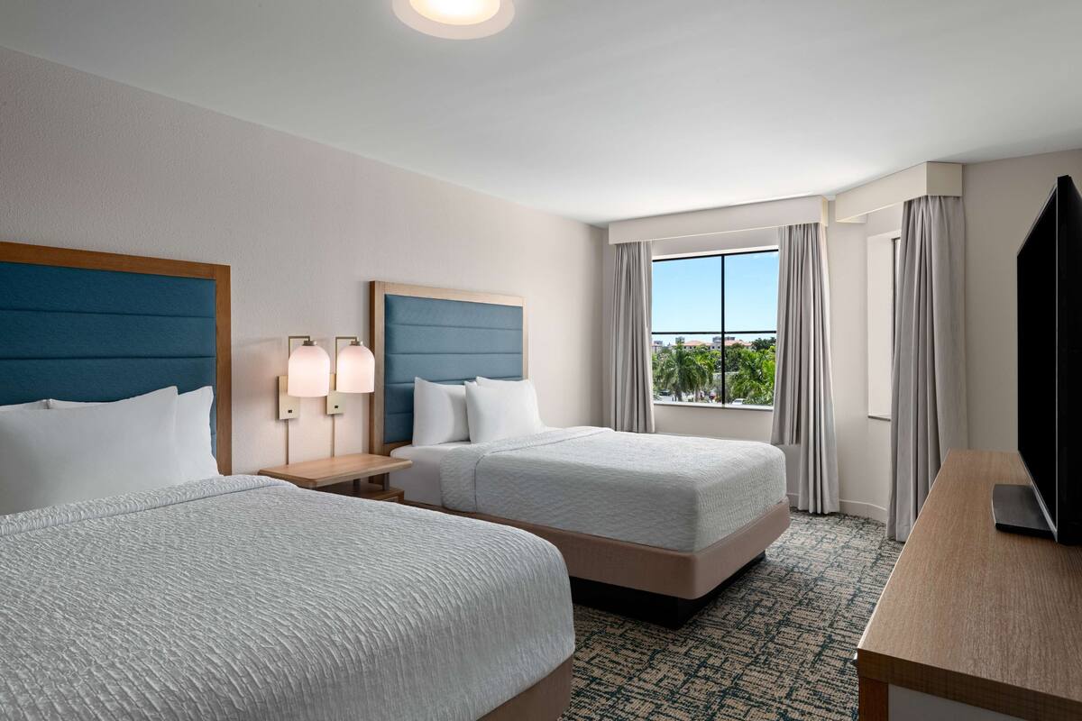 Habitación de hotel con dos camas, televisión, escritorio y ventana con vistas al exterior.