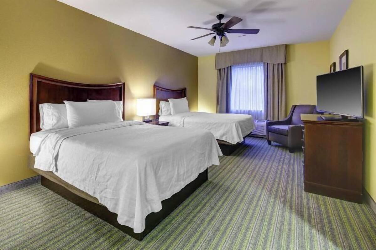 Habitación de hotel con dos camas, un televisor, un escritorio y un ventilador de techo.