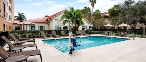 A pool area with lounge chairs and umbrellas, surrounded by buildings and palm trees.