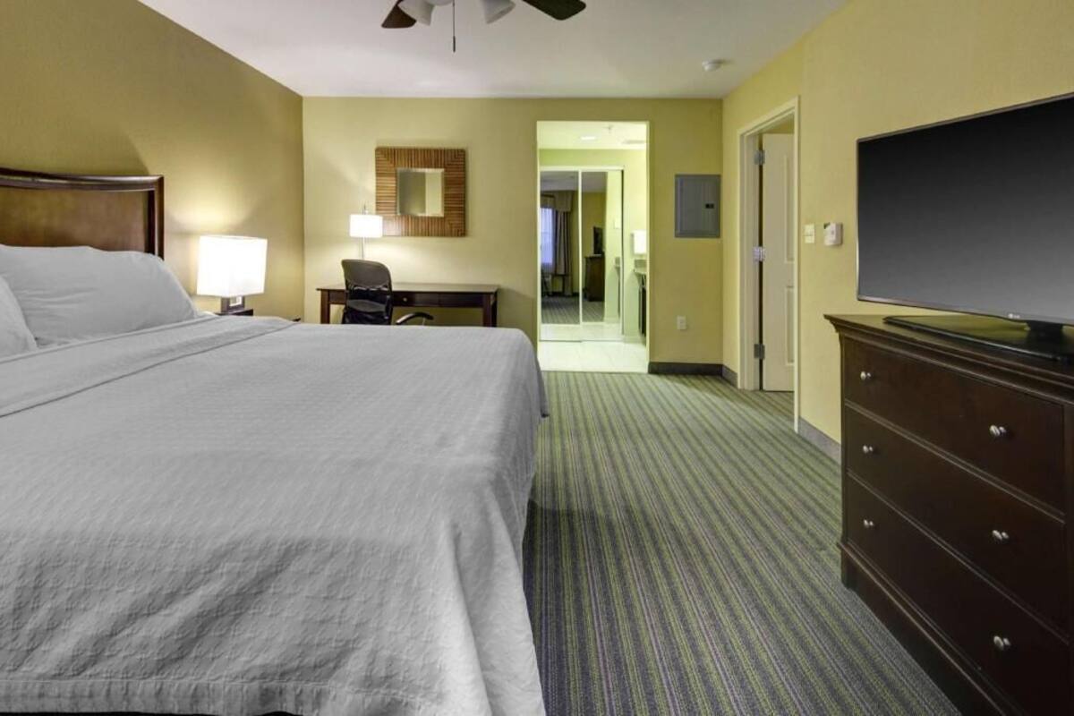 Una habitación de hotel con una cama, un escritorio, una silla, un aparador y un televisor.