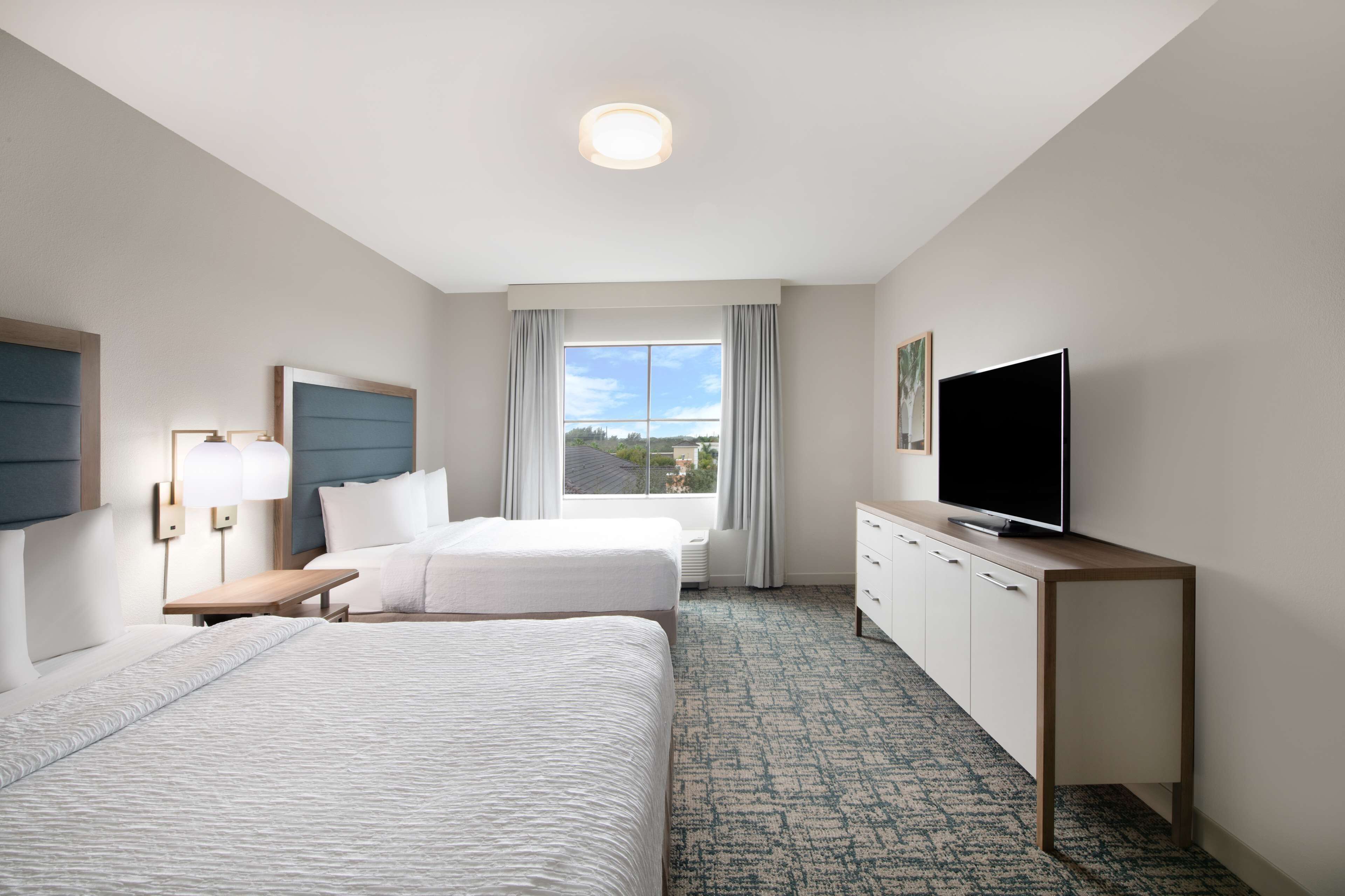A hotel room with two beds, a TV, a desk, and a window with curtains.