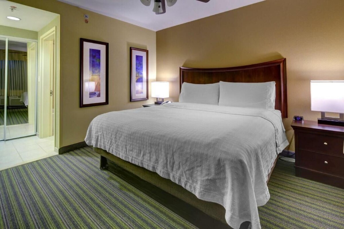 Habitación de hotel con una cama grande, dos lámparas de noche, un cabecero de madera y una puerta que da a un balcón.