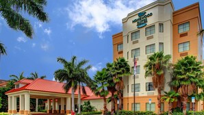 A hotel with a red-roofed entrance, palm trees, and a clear blue sky. - Homewood Suites West Palm Beach (West Palm Beach)