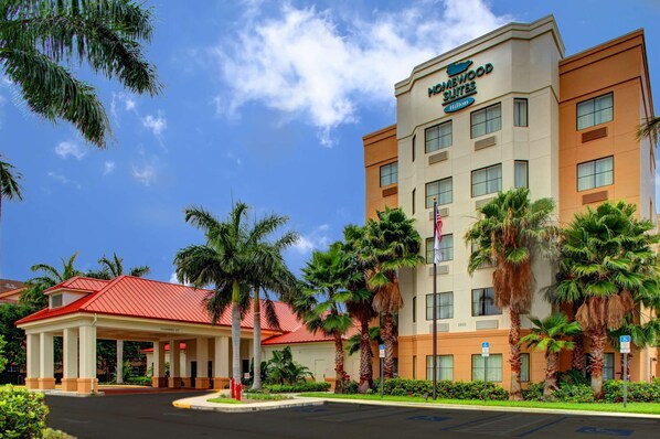 A hotel with a red-roofed entrance, palm trees, and a clear blue sky. - Homewood Suites West Palm Beach (West Palm Beach)