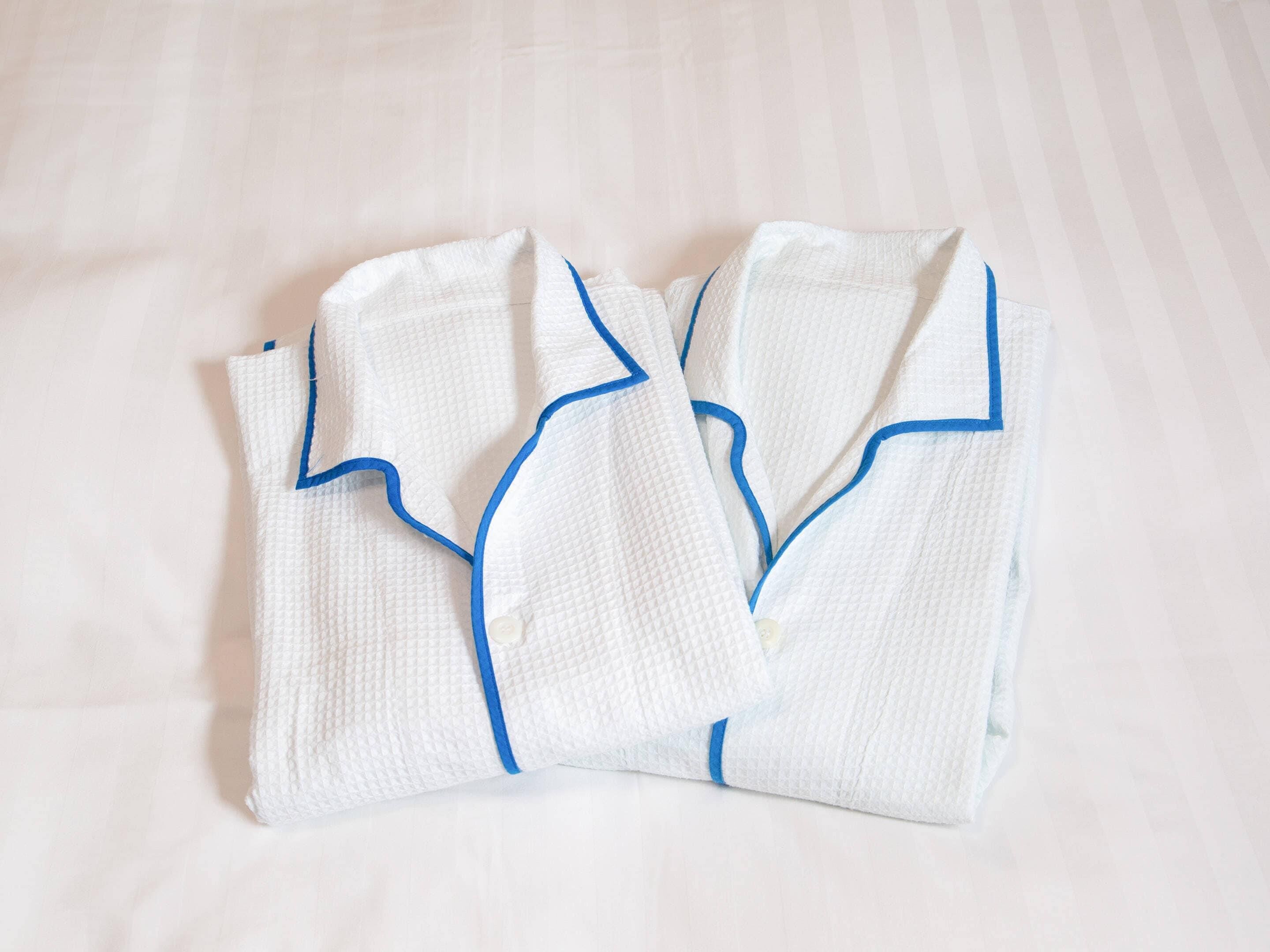 Two neatly folded white robes with blue trim on a white bedspread.