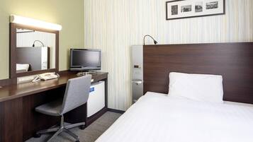Hotelkamer met een bed, een bureau met een computer, een telefoon, een spiegel, een wandklok en een ingelijste foto.