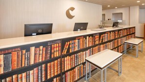 Una recepción con computadoras, un elemento decorativo en forma de C en la pared y una estantería llena de libros.