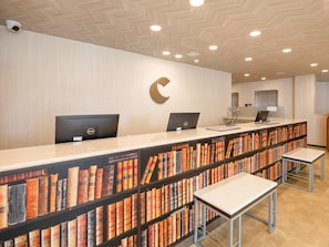 Una recepción con computadoras, un elemento decorativo en forma de C en la pared y una estantería llena de libros.