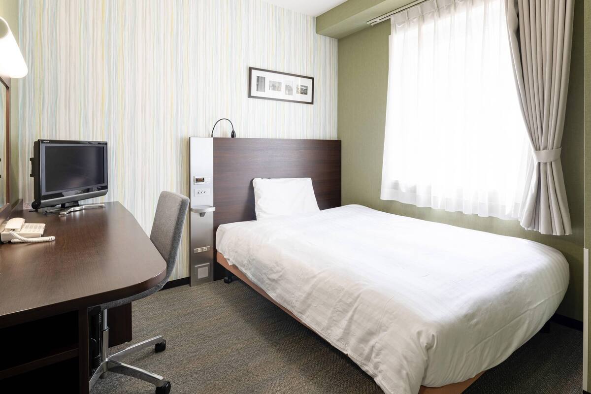 A hotel room with a bed, a desk with a computer, a telephone, and a picture frame on the wall.