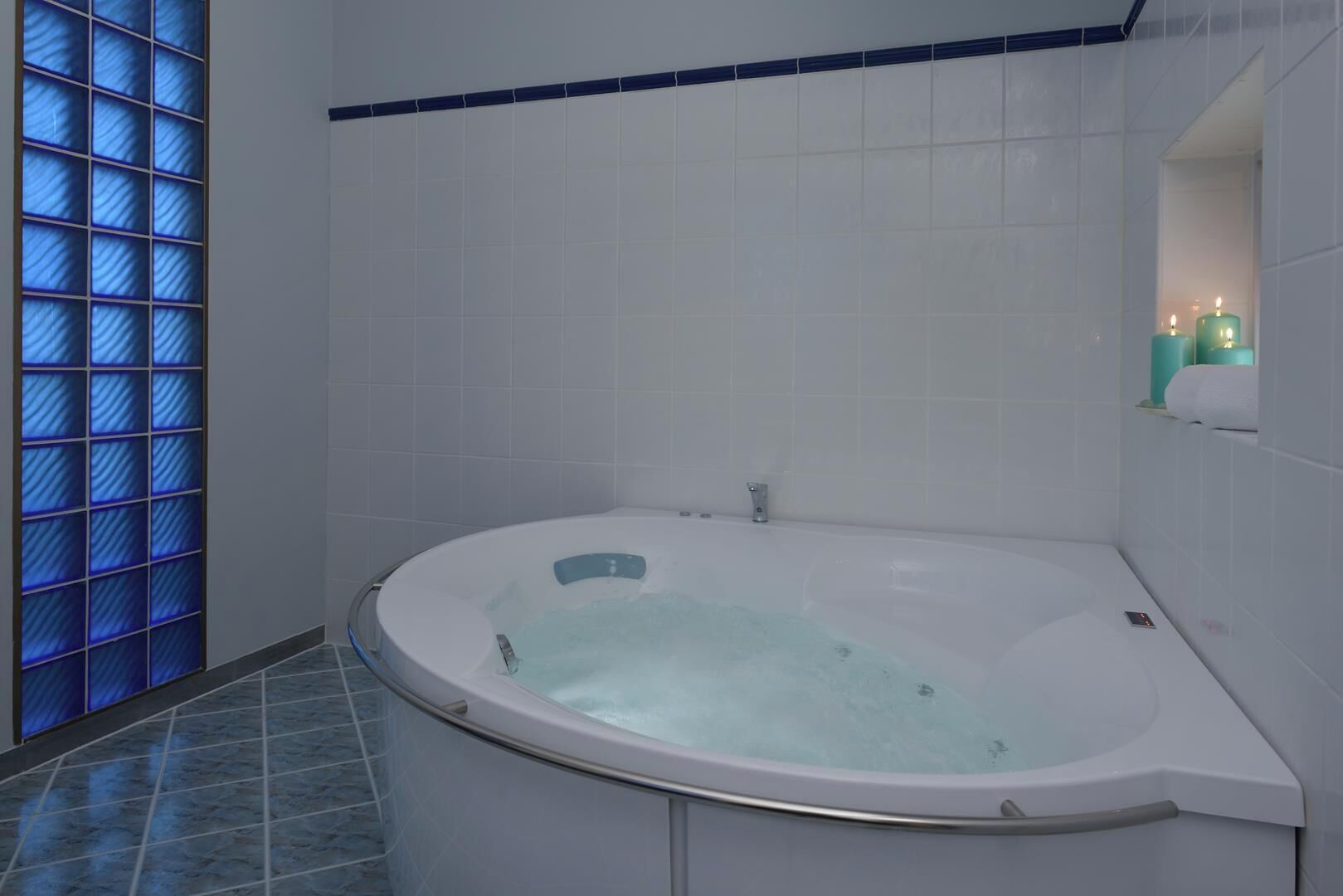 A modern bathroom with a freestanding bathtub, white tiles, and a glass partition with blue lighting.