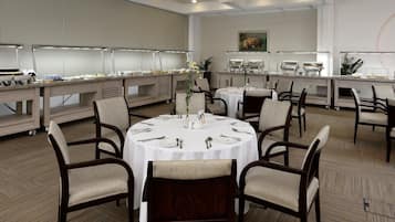 A buffet setup with multiple tables and chairs, a large painting on the wall, and a wooden floor.