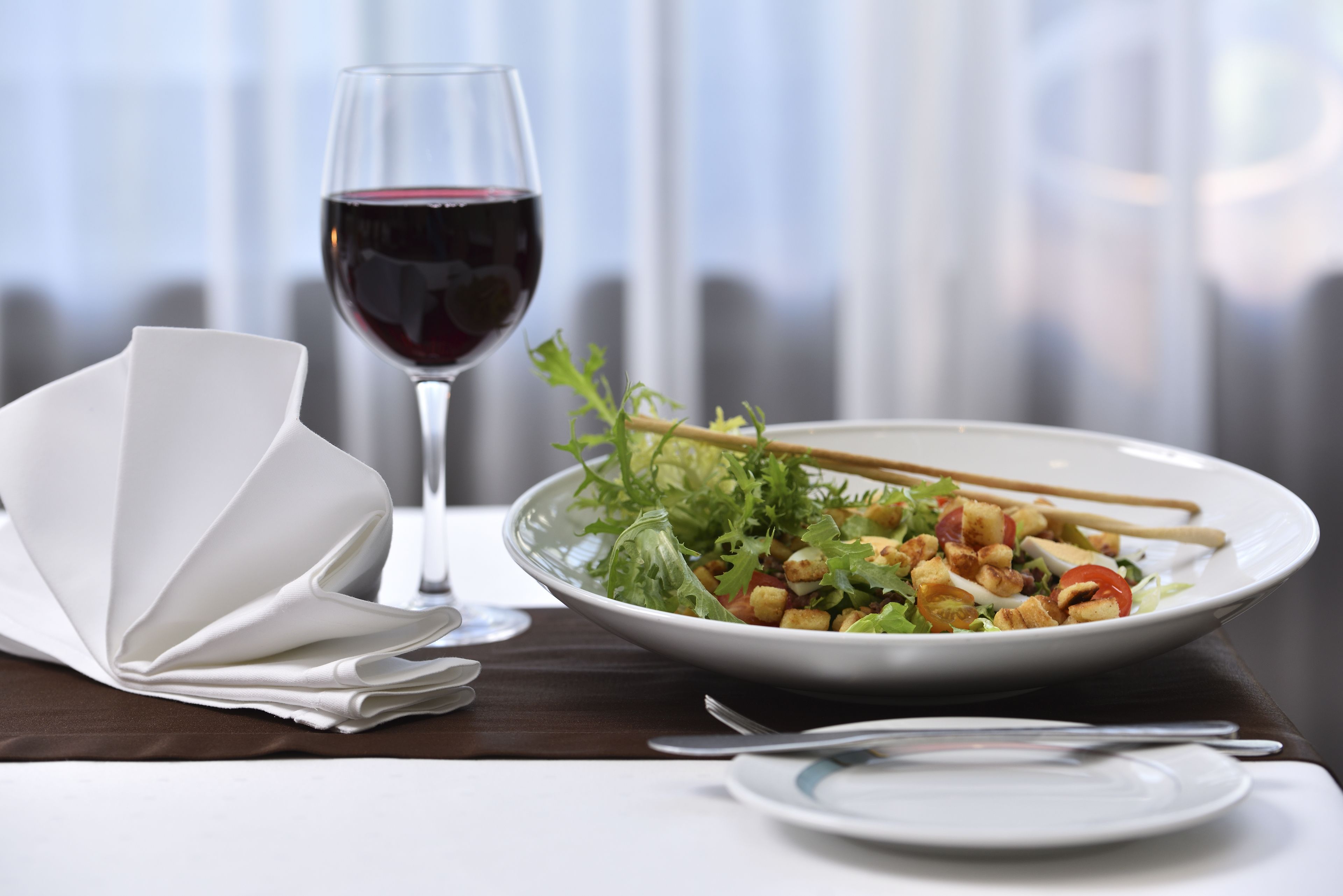 Ein Esstisch mit Salat, einem Glas Rotwein und einem gefalteten Servietttuch.