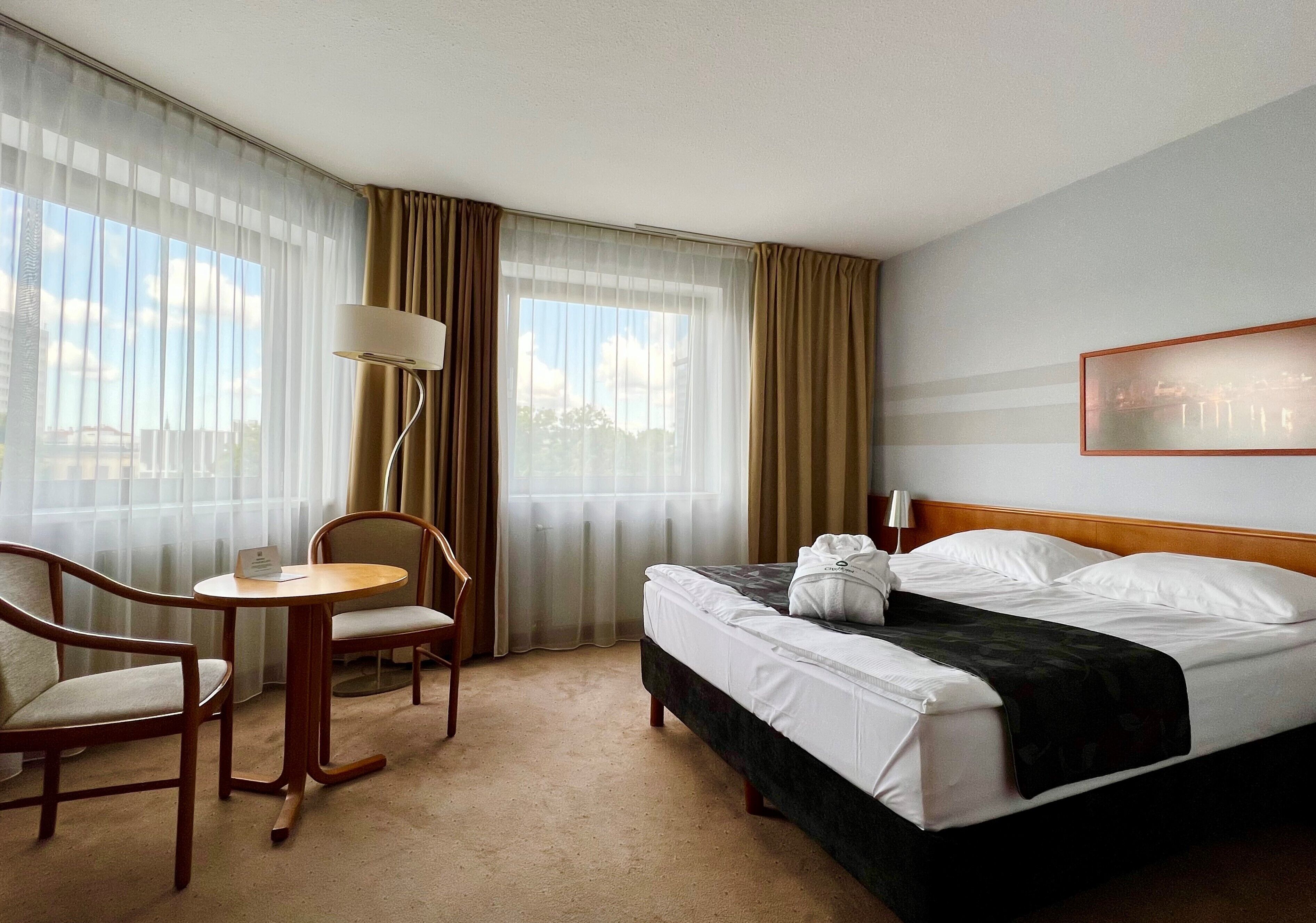 A hotel room with a bed, a chair, a small table, and a lamp.