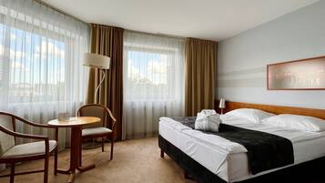 A hotel room with a bed, a chair, a small table, and a lamp.