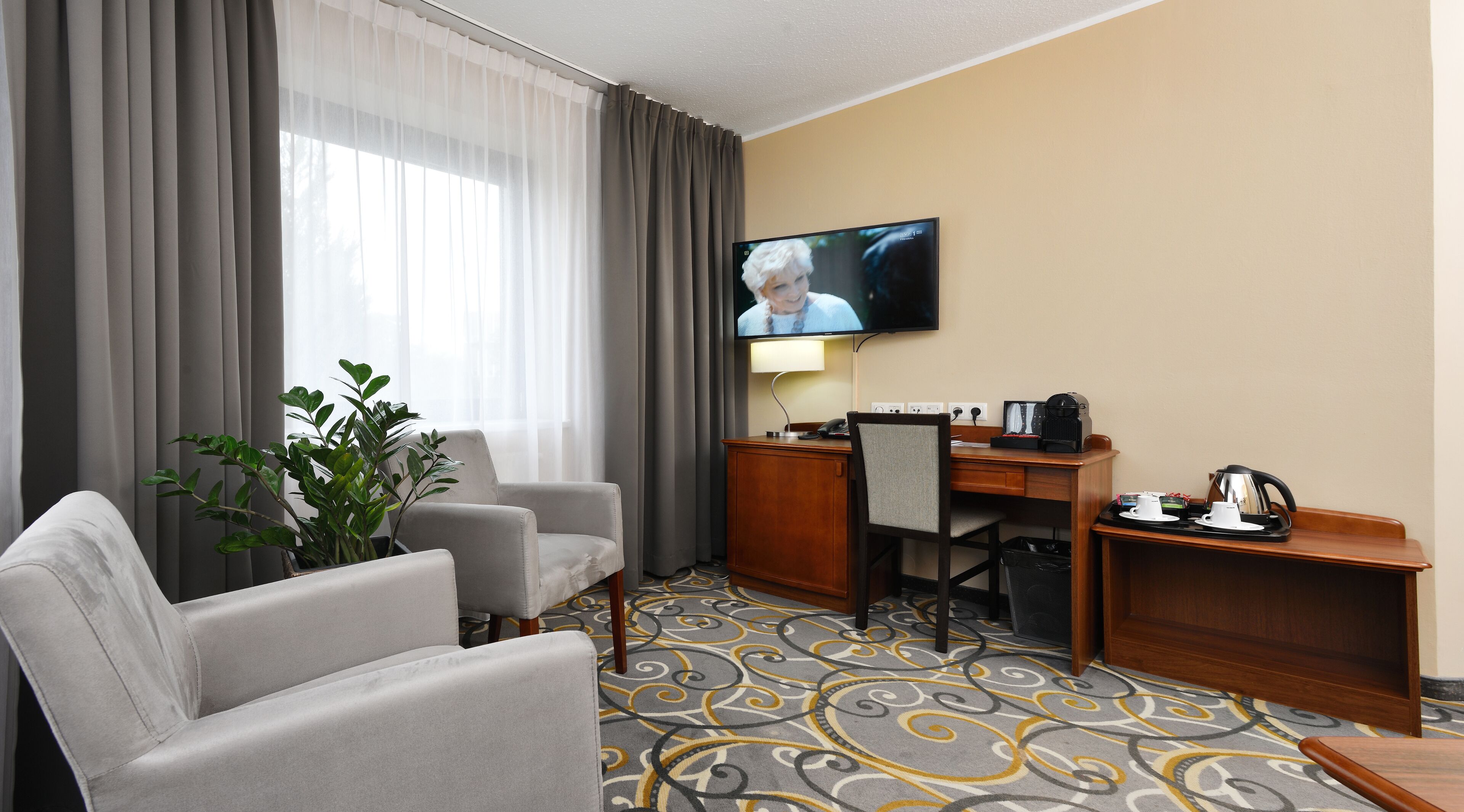A hotel room with a sofa, a desk with a computer, a television, and a coffee maker.