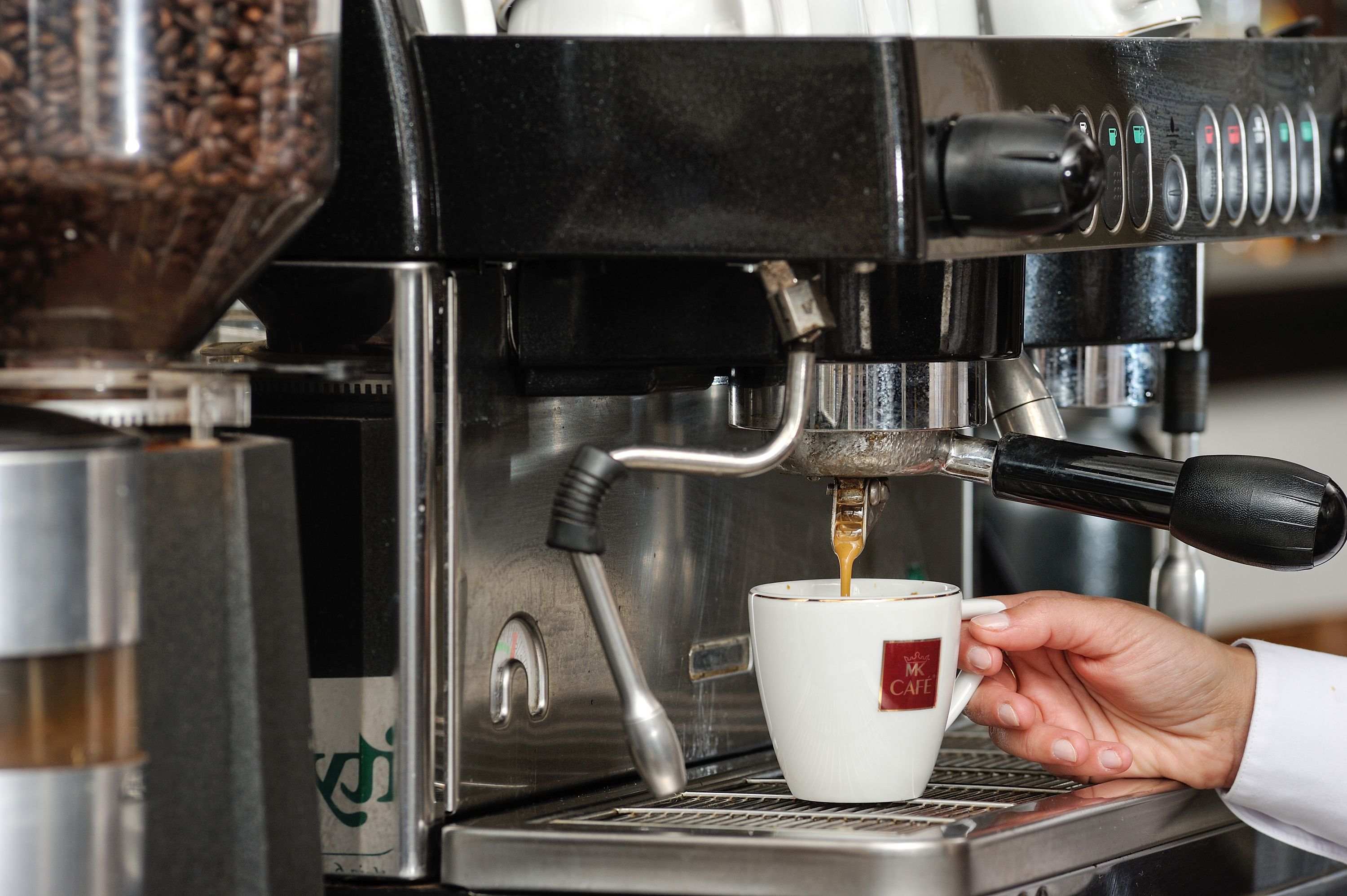 Eine Hand hält eine Tasse, während eine Kaffeemaschine Kaffee einfüllt.