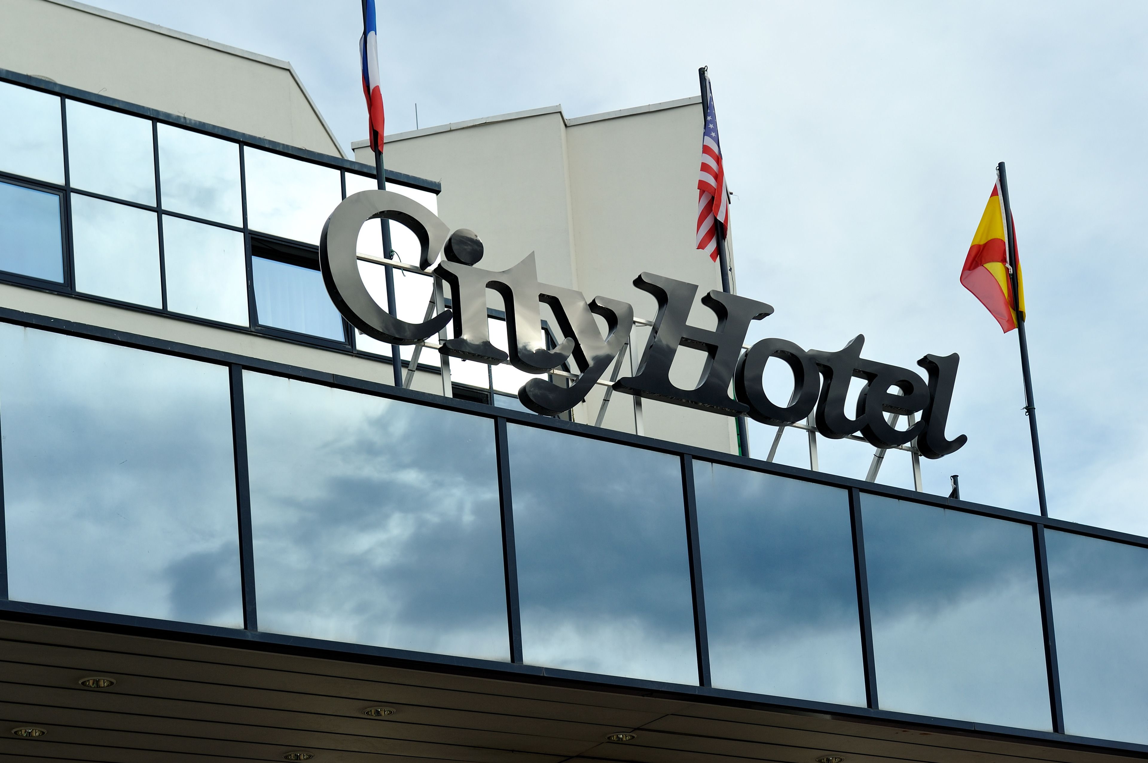 Une enseigne d’hôtel portant le nom « City Hotel » et deux drapeaux, un américain et un autre rouge et jaune.