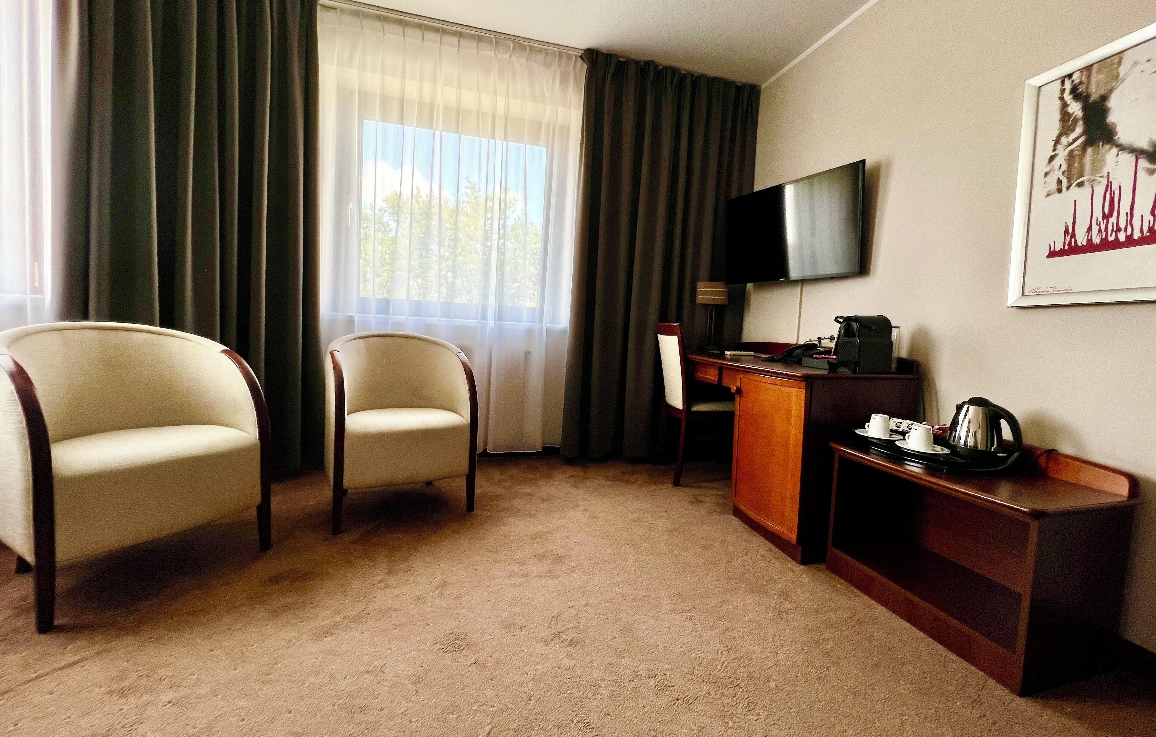 A hotel room with two armchairs, a desk with a television, a coffee maker, and a tray with cups.