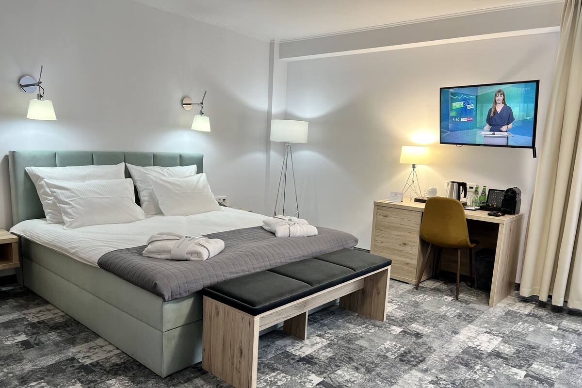 Una habitación de hotel con cama, mesitas de noche, un escritorio con silla, televisor y lámpara.