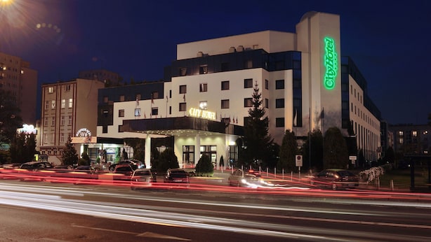 Un hotel urbano con fachada moderna, varios pisos y un llamativo letrero verde.
