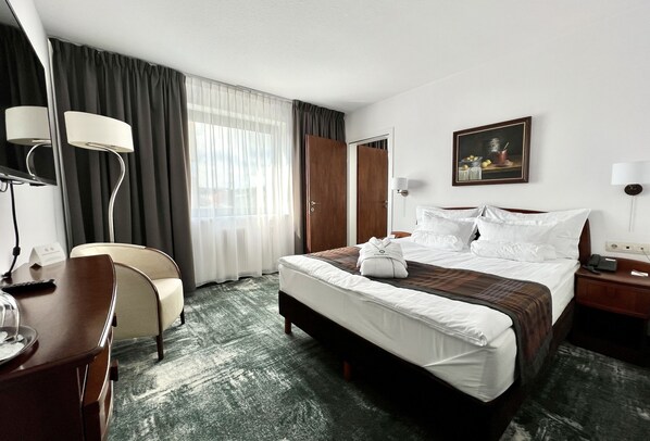 Habitación de hotel con cama, mesita de noche, lámpara, silla y un cuadro en la pared.