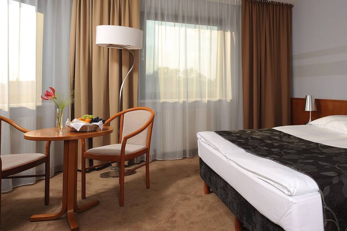 Una habitación de hotel con una cama, un escritorio con una silla, una lámpara y un cuadro en la pared.
