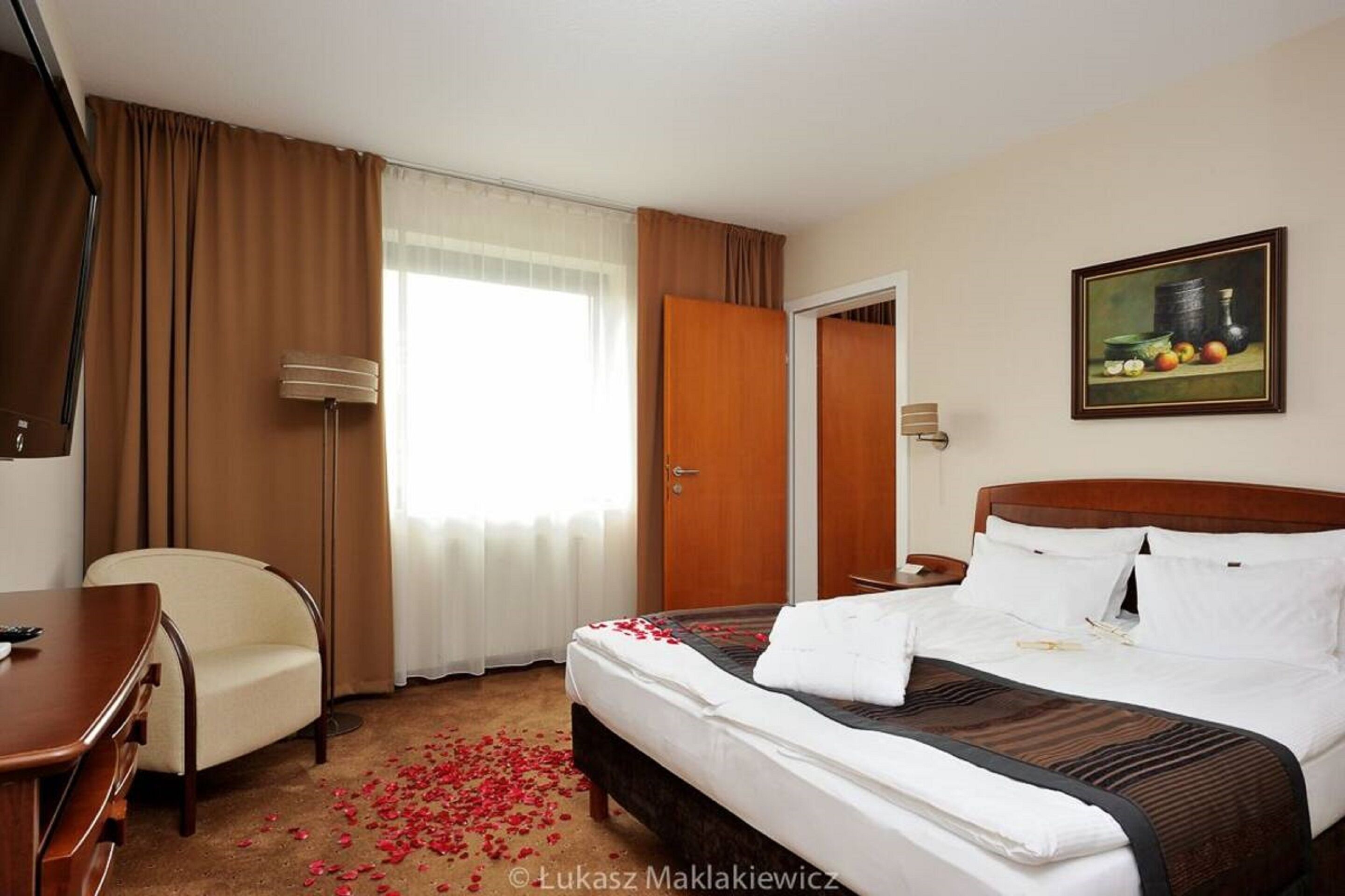A hotel room with a bed, a desk, a chair, a painting, and a door.