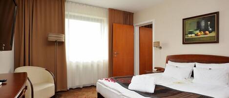A hotel room with a bed, a desk, a chair, a painting, and a door.