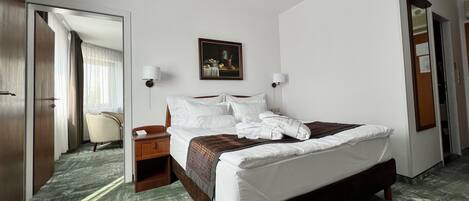 A hotel room with a large bed, a desk, a chair, and a painting on the wall.