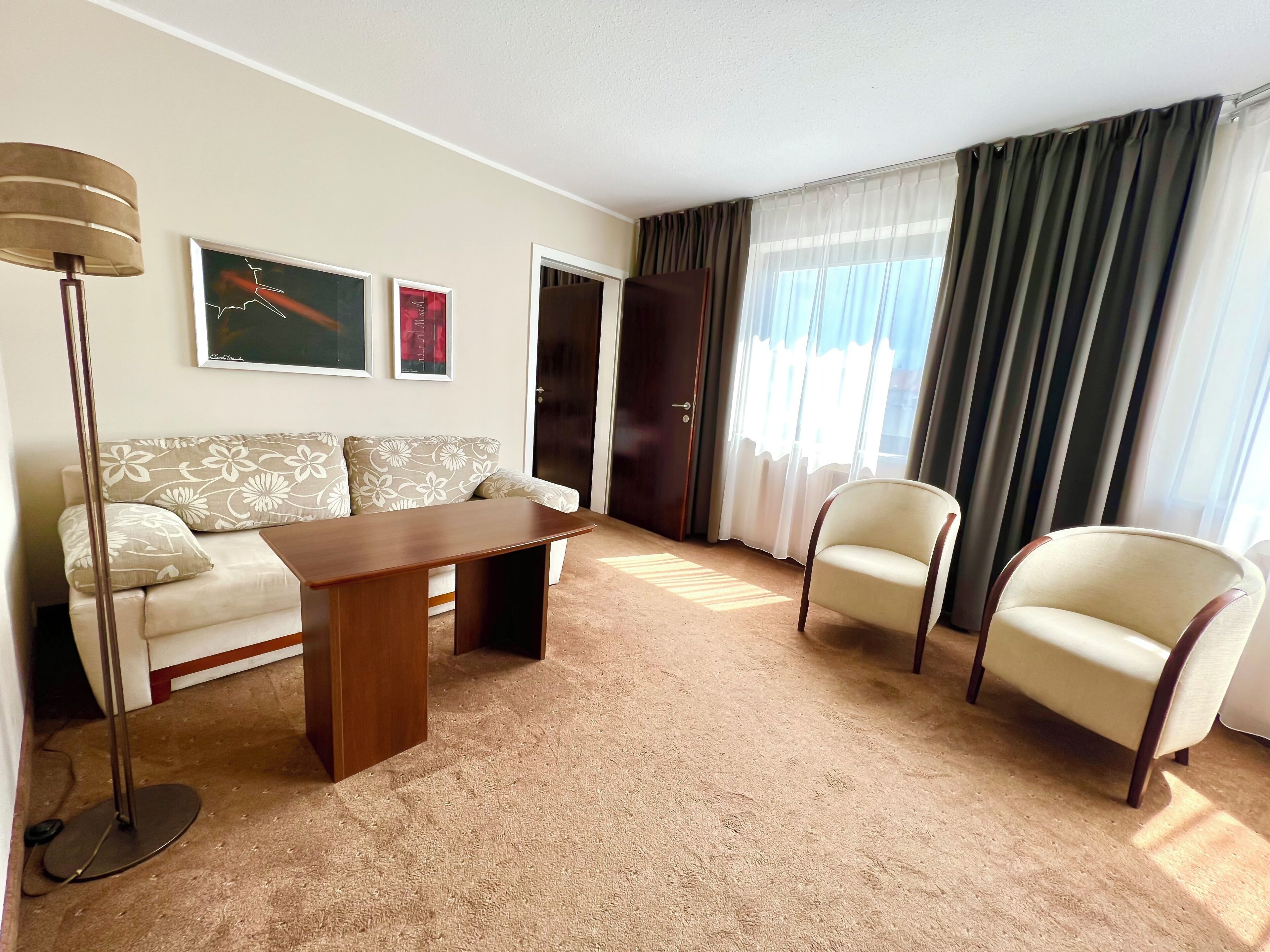 Una sala de estar con un sofá, dos sillones, una mesita de centro, una lámpara de pie y una puerta.