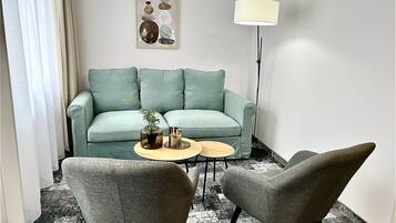 Una sala de estar moderna con un sofá azul aguamarina, dos sillones, una mesita de centro, una lámpara de pie y un elemento decorativo en la pared.