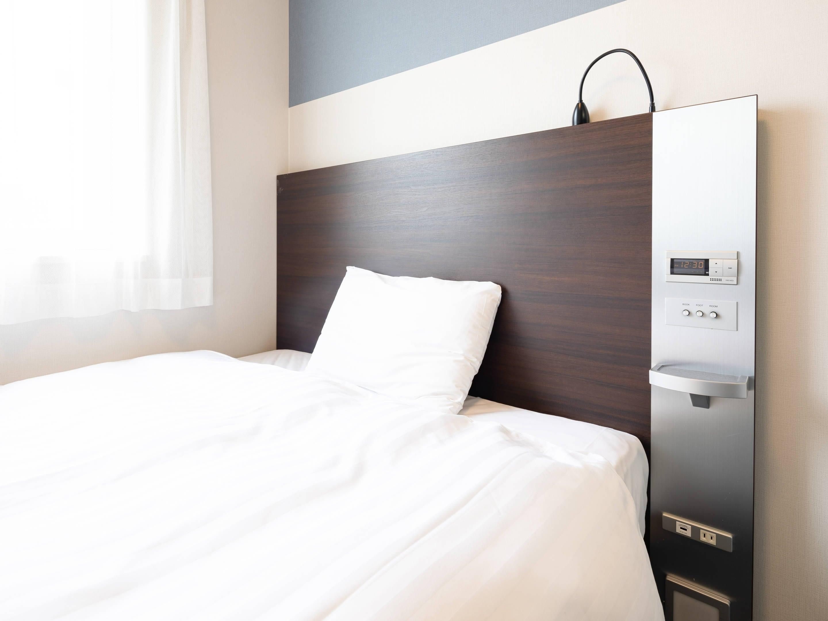 Una habitación de hotel con una cama, un reloj digital y un panel de control con botones para configurar la estancia.