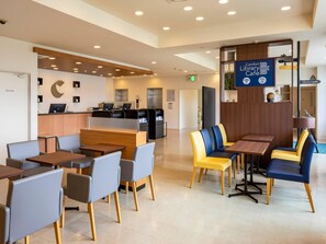 Un café moderno en una biblioteca con mesas y sillas, una zona de recepción y un panel informativo digital.