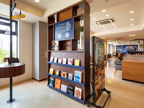 Um café moderno em uma biblioteca, com uma estante de madeira exibindo livros, um mapa na parede e uma área de estar com mesas e cadeiras.