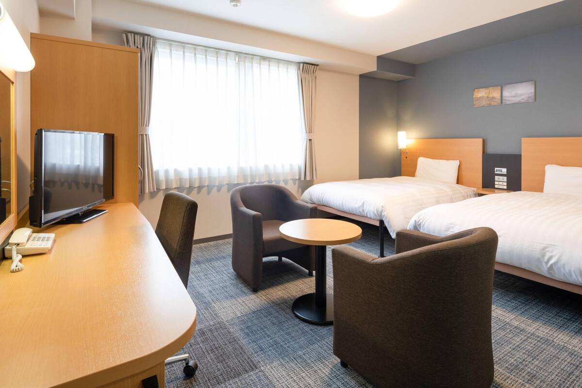 Ett hotellrum med ett skrivbord, två stolar, en säng och en tv.