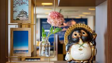 Una repisa decorativa con una pintura tradicional de un edificio japonés, un florero con una flor rosa y una figurita de cerámica de un búho.